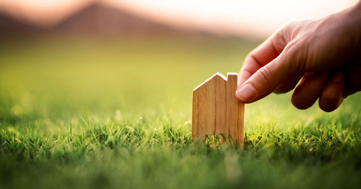 concept of small estate probate hand touching little wood shape of house in grass